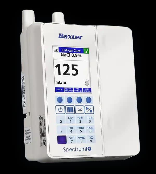A medical infusion pump with a digital display showing Critical Care NaCl 0.9% and 125 mL/hr. The device has several buttons, a screen, and visible antennae on top. The brand name Baxter and model Spectrum IQ are printed on the device.